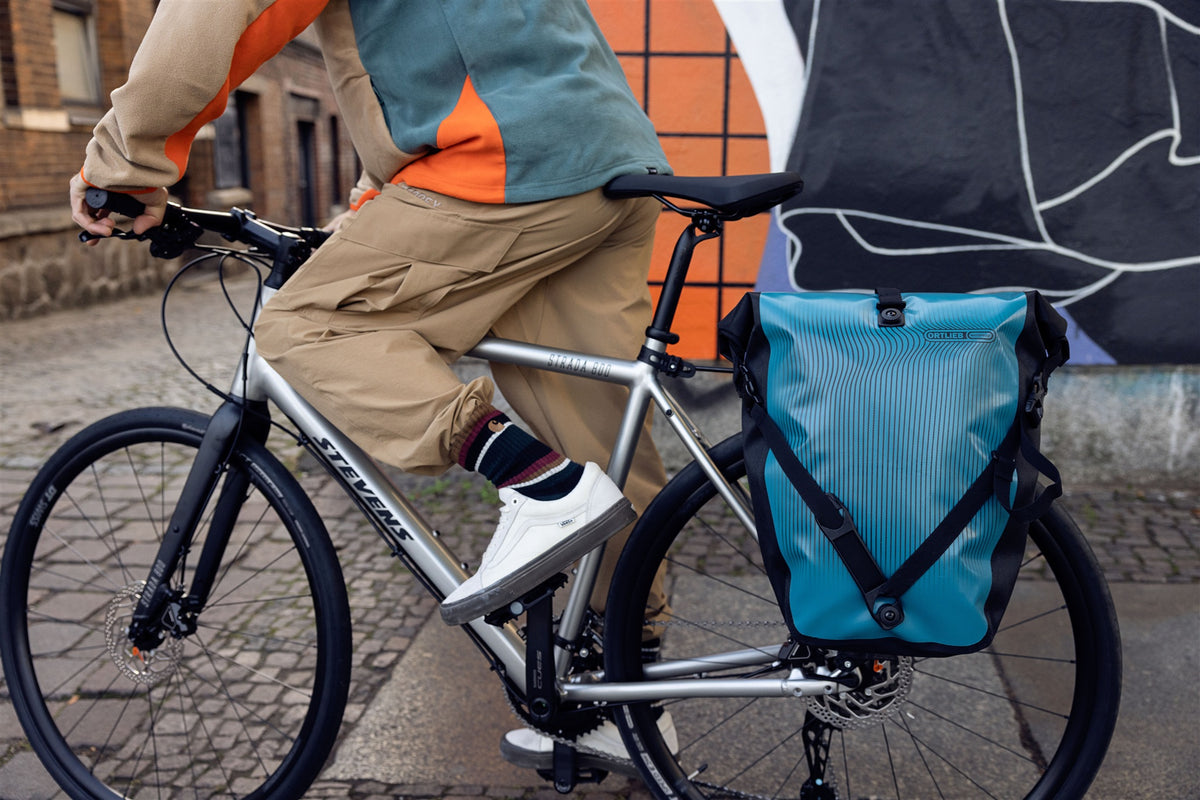 ortlieb back-roller design bag in petrol blue on bike rack in urban setting