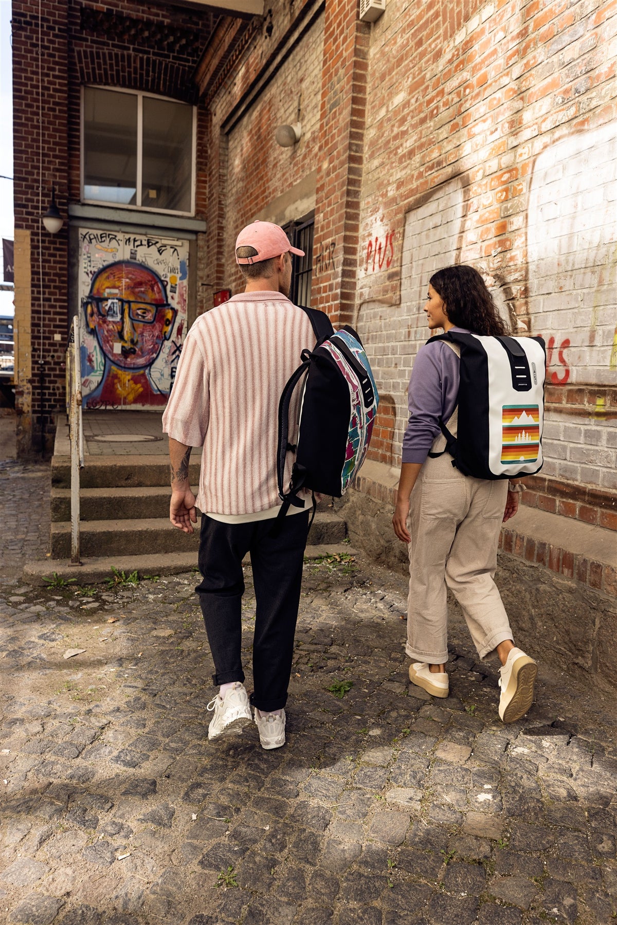 Two people with ORTLIEB Velocity Design backpacks walking along urban backdrop
