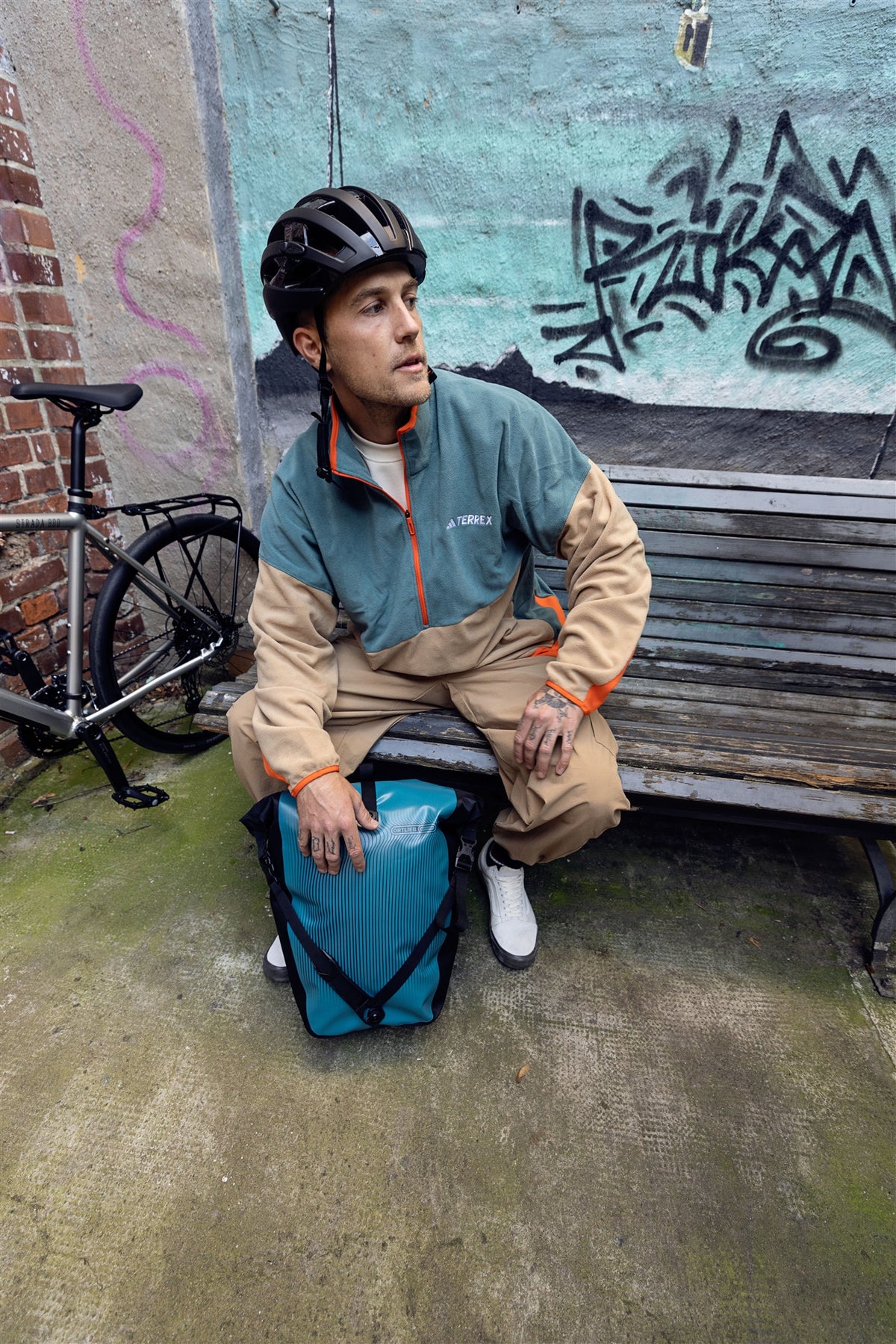 man wearing bike helmet beside bicycle holding ORTLIEB Back-Roller Design bag in petrol blue