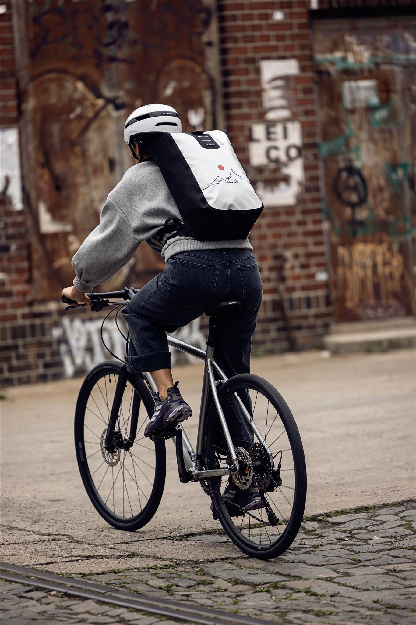 Woman sitting on metal stairs with white black ORTLIEB Velocity Design backpack featuring red sun
